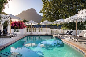 Un espace piscine agrémenté de chaises longues et de parasols, entouré d’une clôture blanche et de verdure.