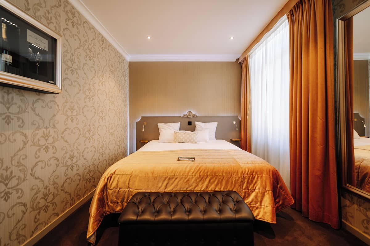 A hotel room with a large bed, a headboard, a bench, a television, and curtains.
