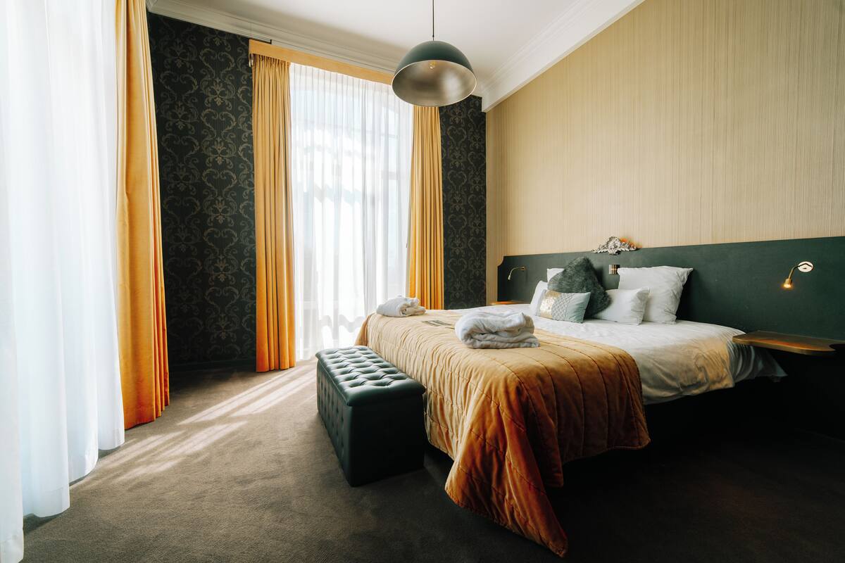 A hotel room with a large bed, a bench, and a hanging light fixture.