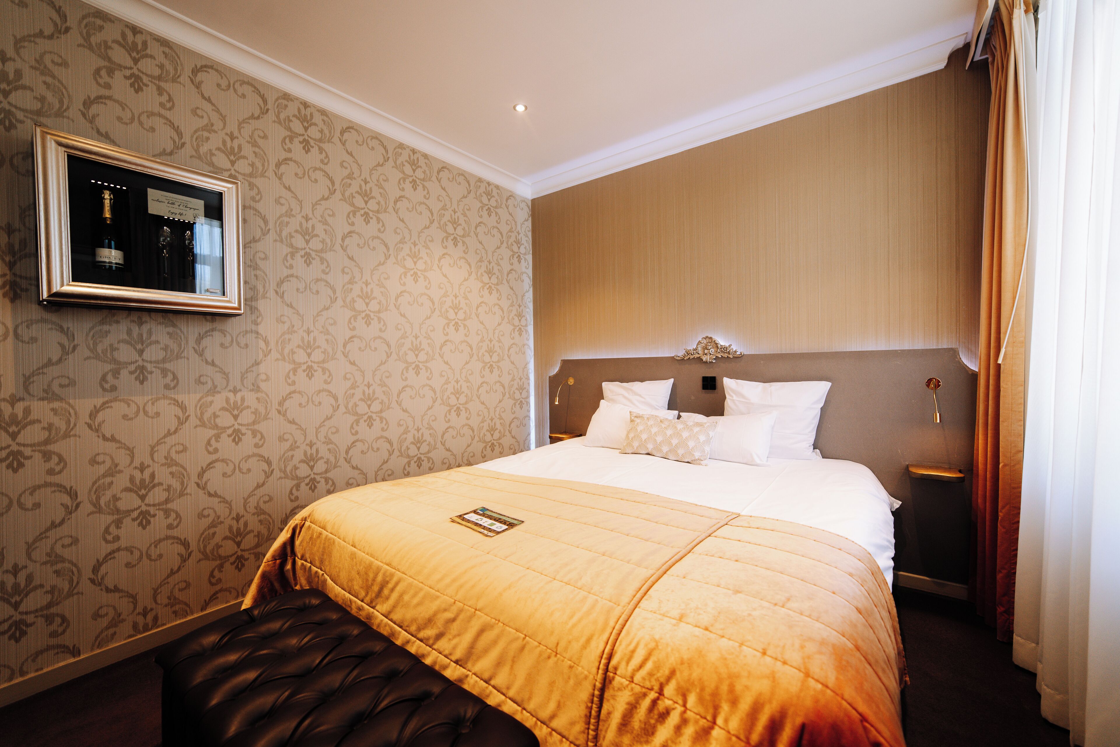 A hotel room with a large bed, a headboard, a bedside table, and a wall-mounted mirror.
