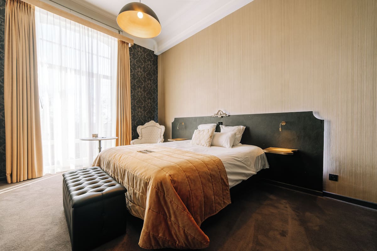 A hotel room with a large bed, a bedside table, a chair, and a window with curtains.