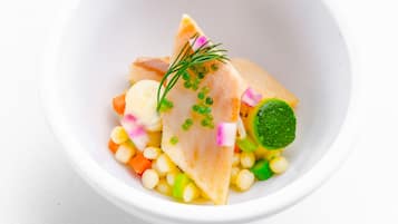 A white bowl containing a seafood dish with various vegetables and garnishes.