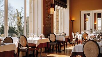 Un ristorante con diversi tavoli apparecchiati, ampie finestre e una parete in mattoni.
