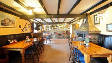 Un interno di pub tradizionale con tavoli di legno, pareti in pietra e travi a vista.