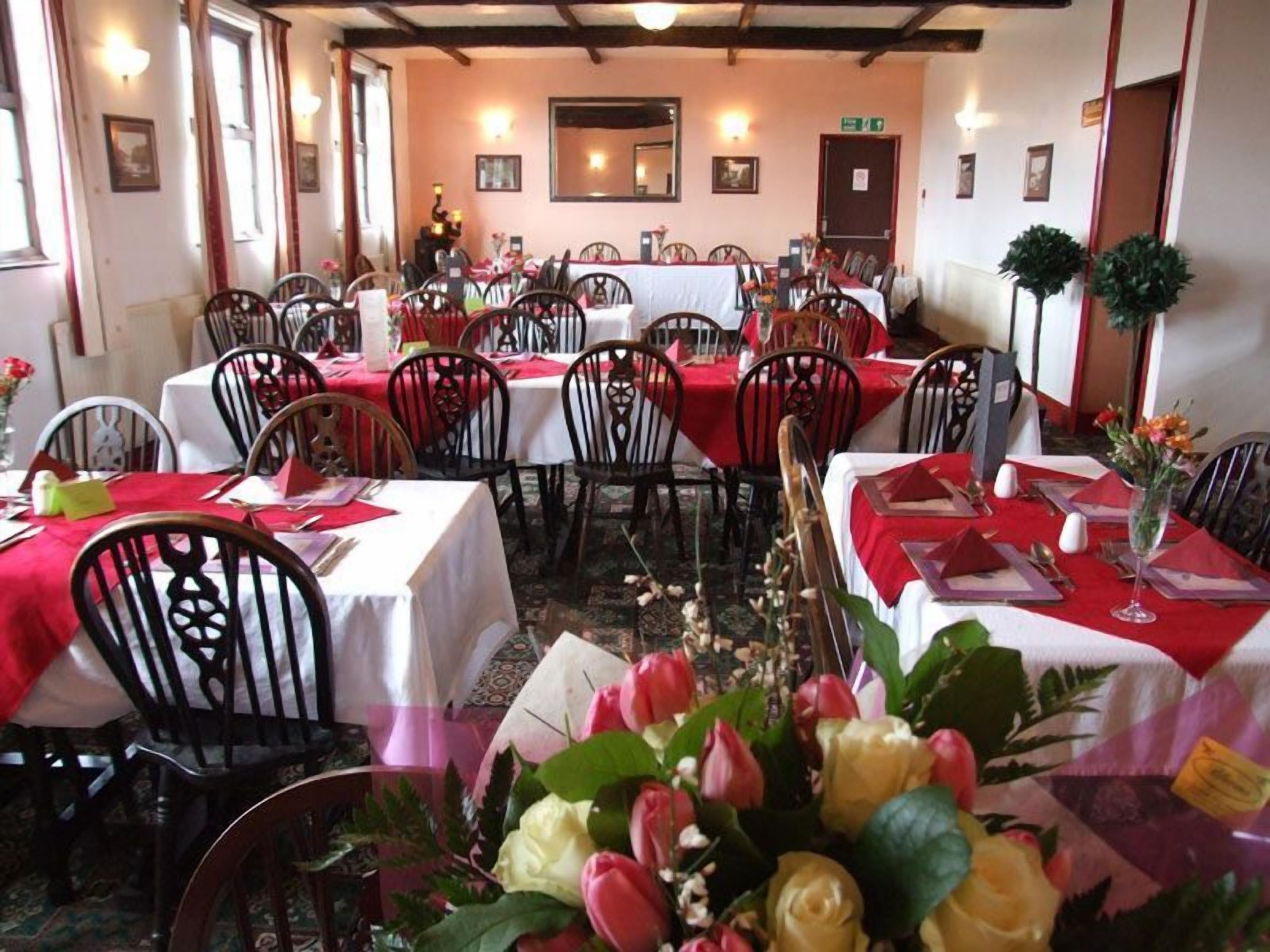 A dining area with multiple tables set for service, each covered with a white tablecloth and red napkins.