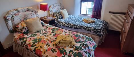 Un dormitorio con dos camas, alfombra roja, cómoda de madera y una ventana con cortinas.