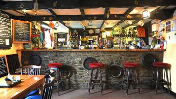 Una zona de bar con taburetes de madera, pared de piedra y una pizarra con el menú.