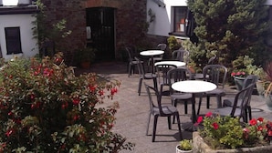 An outdoor patio with stone flooring, surrounded by potted plants and red flowers. - The West Country Inn (Bideford)
