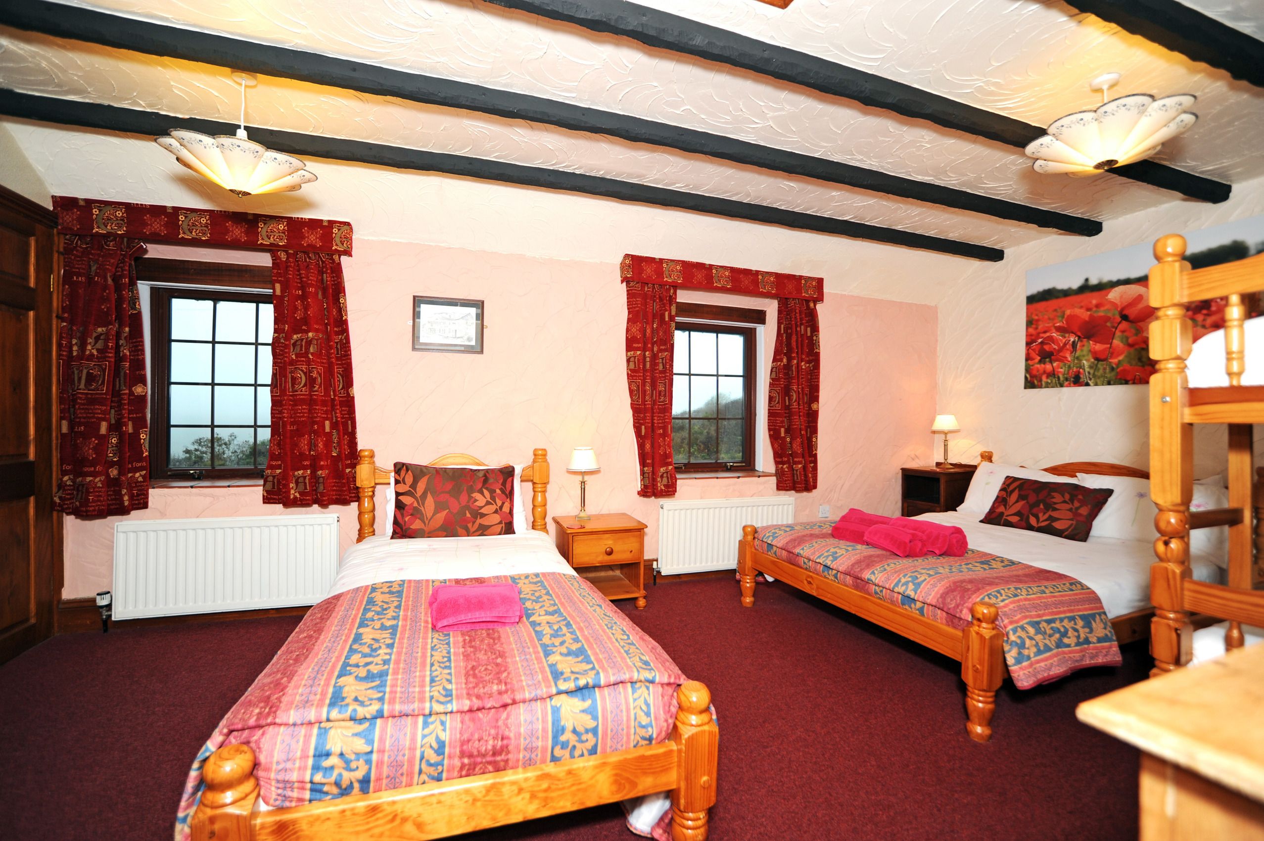 A traditional room with two wooden beds, red curtains, a white radiator, and a wooden ceiling with exposed beams.
