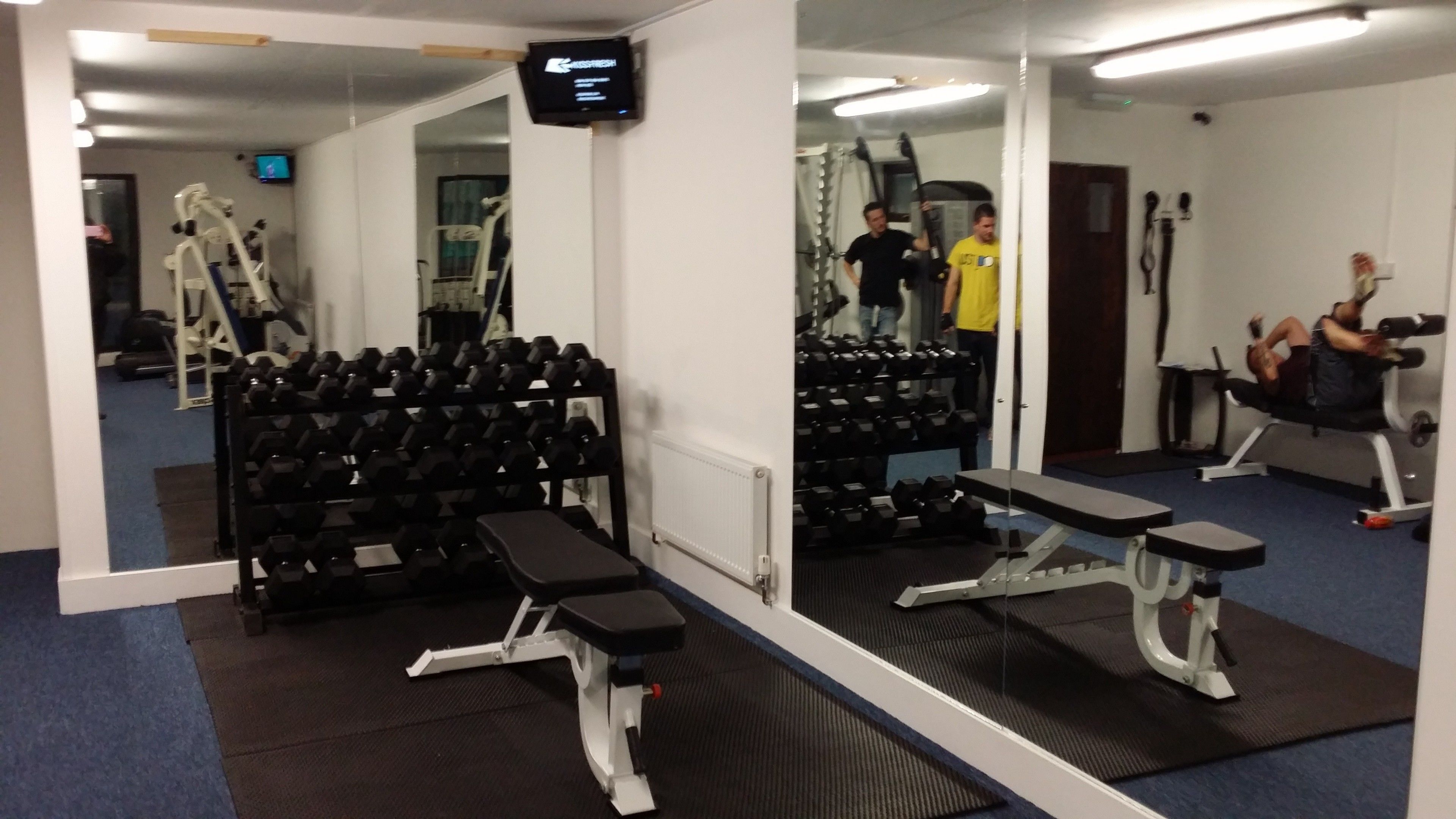 A gym with exercise equipment, mirrors, and a television screen.
