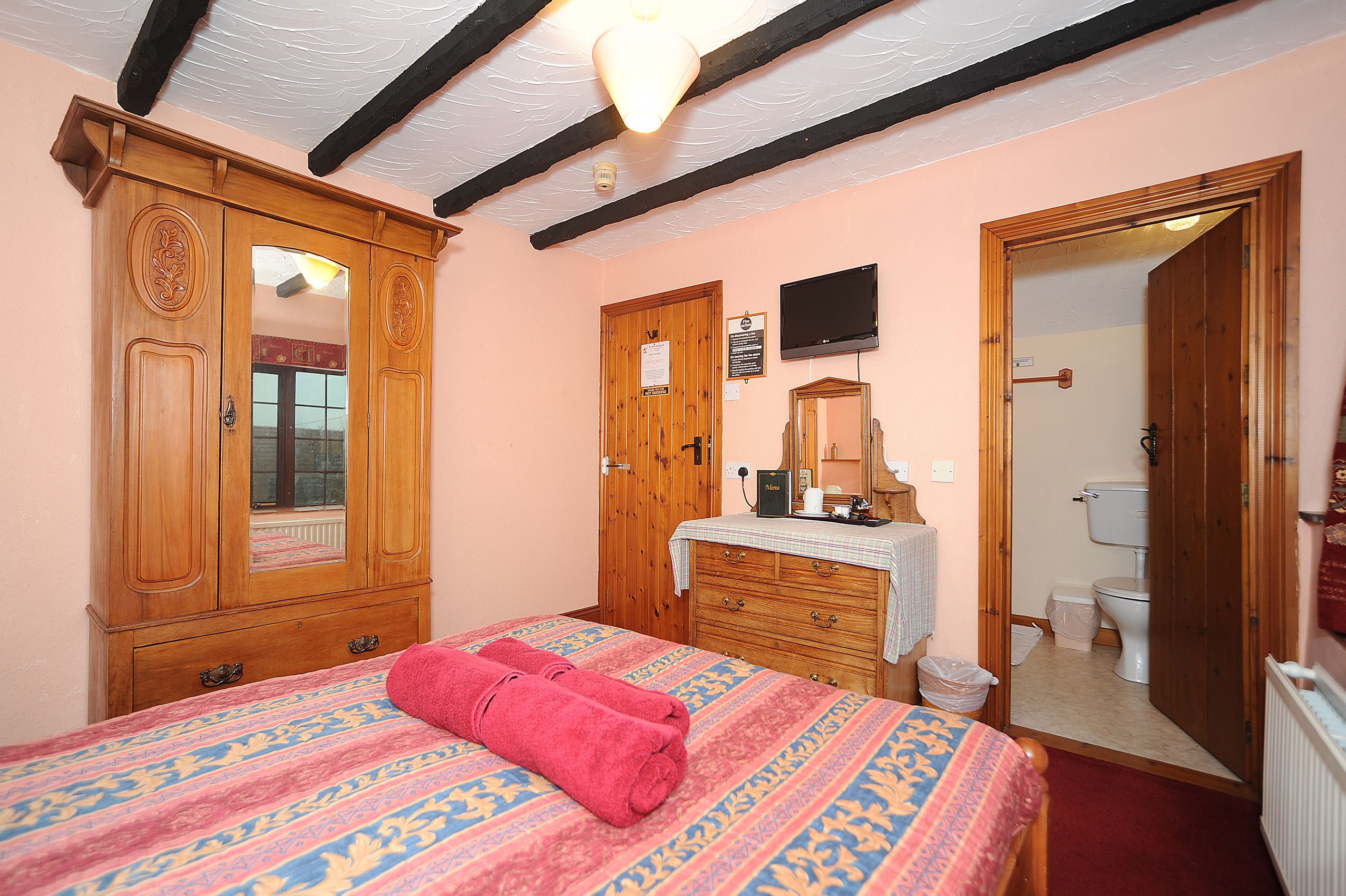 Une chambre à coucher comprenant un lit, une armoire en bois, une commode, un miroir et un téléviseur.
