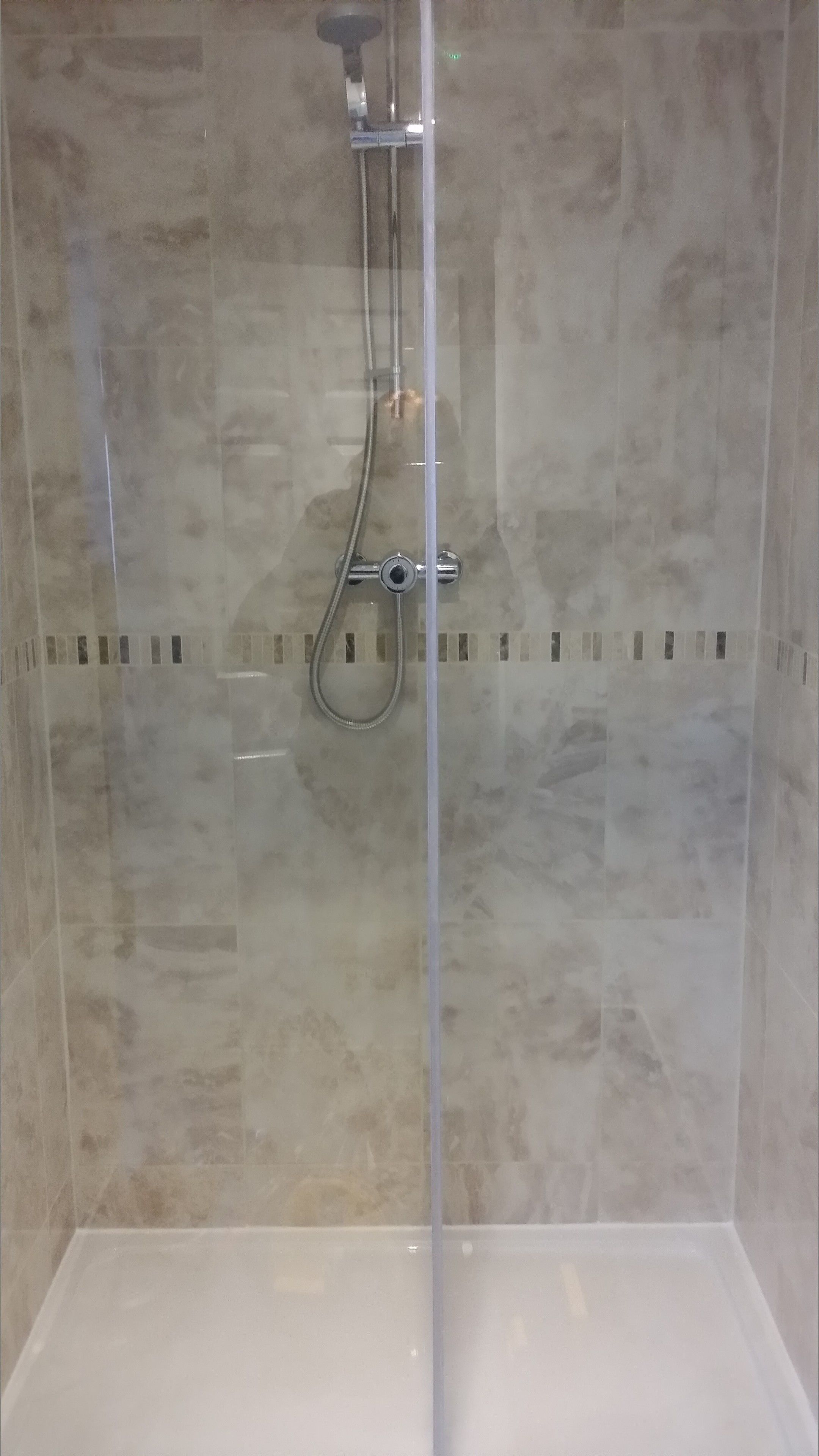 A glass-enclosed shower with a handheld showerhead and a fixed overhead showerhead.