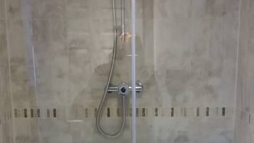 A glass-enclosed shower with a handheld showerhead and a fixed overhead showerhead.