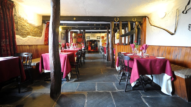 A restaurant with stone flooring, wooden beams, and tables set with red tablecloths. - The West Country Inn (Bideford)