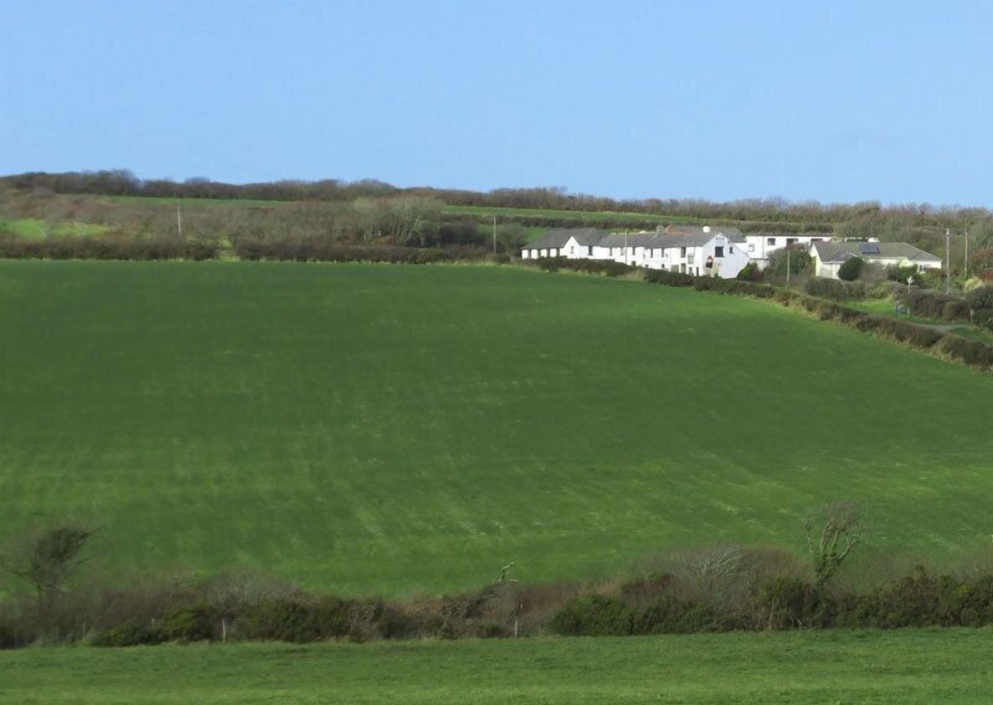 A large green field with a row of white buildings in the background.