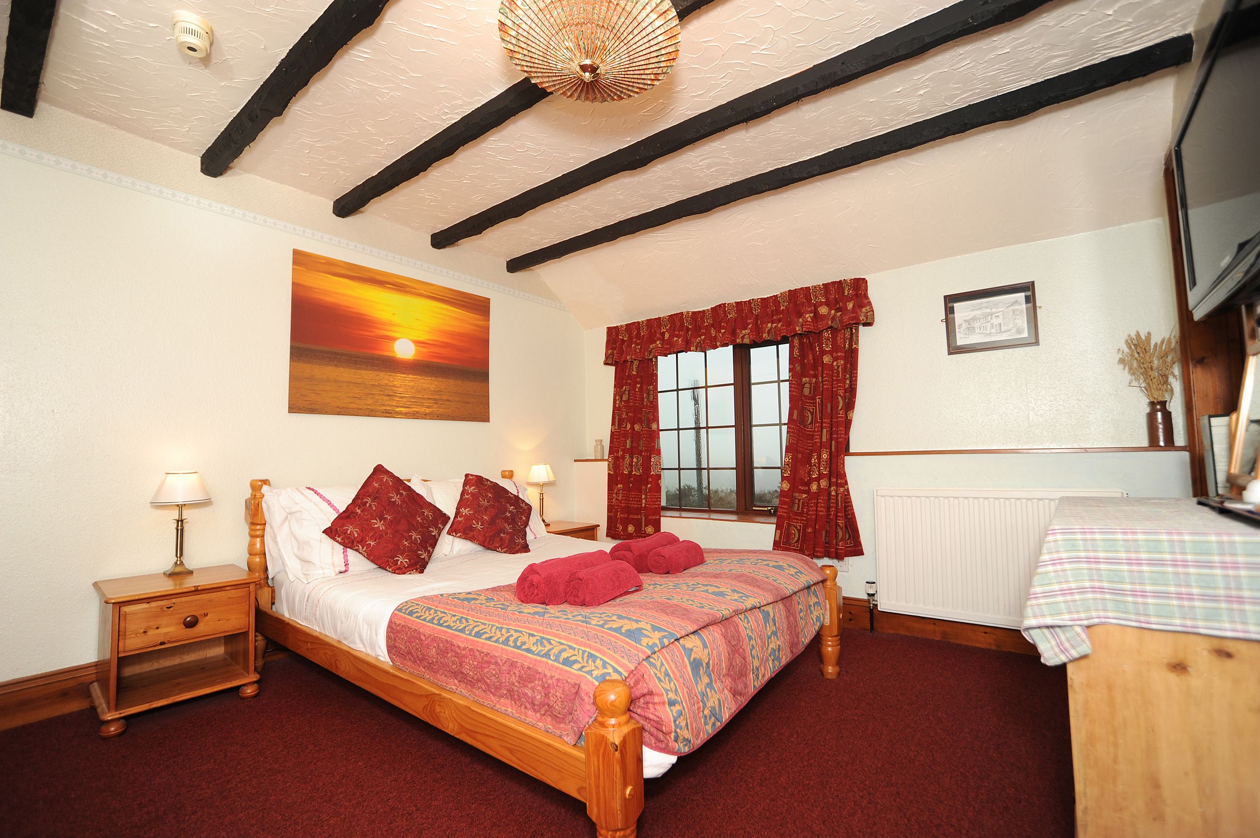 A bedroom with a wooden bed, red curtains, a painting of a sunset, and a radiator.