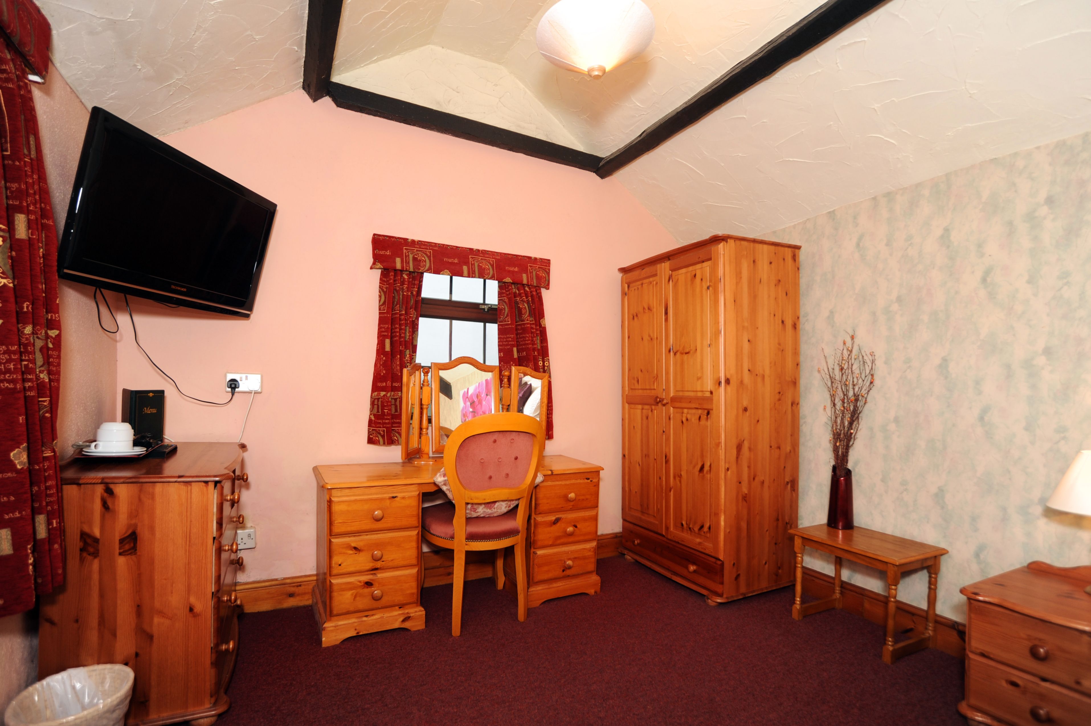 A room with a desk, chair, wardrobe, and a television mounted on the wall.