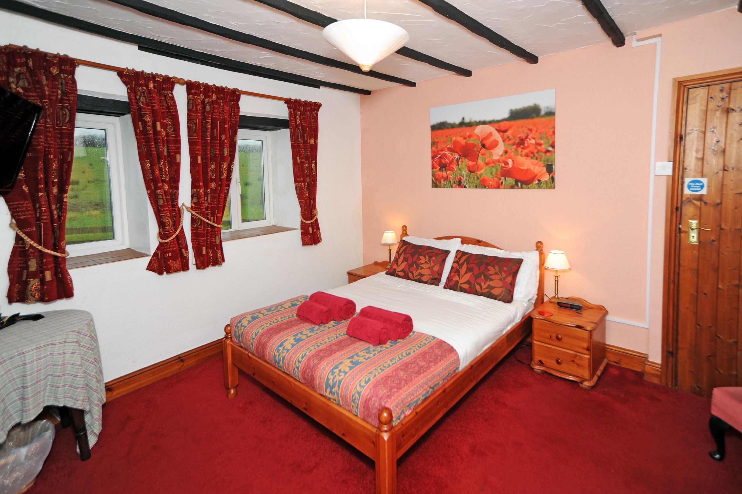 A bedroom with a wooden bed, red curtains, a nightstand with a lamp, and a door with a sign.
