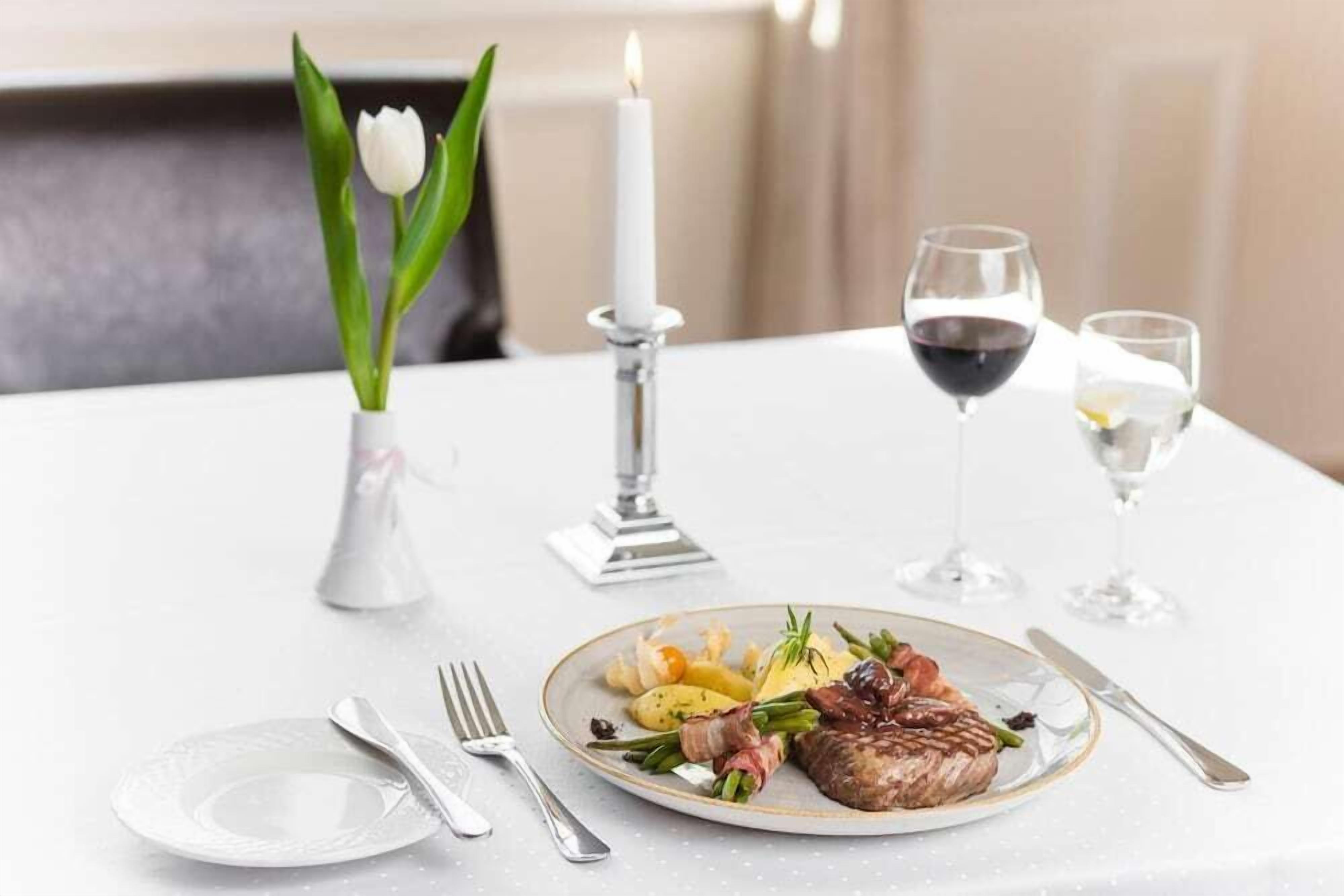A dining table with a plate of food, a candle, and two glasses of wine.
