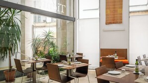Un comedor moderno con mesas y sillas, ventanas amplias y plantas de interior.
