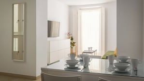Una cocina moderna con una mesa de vidrio para cuatro comensales, armarios blancos y vistas a un balcón con una silla.