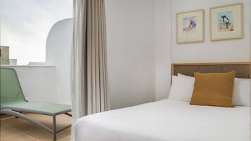 A hotel room with a bed, a chair, and two framed pictures on the wall.