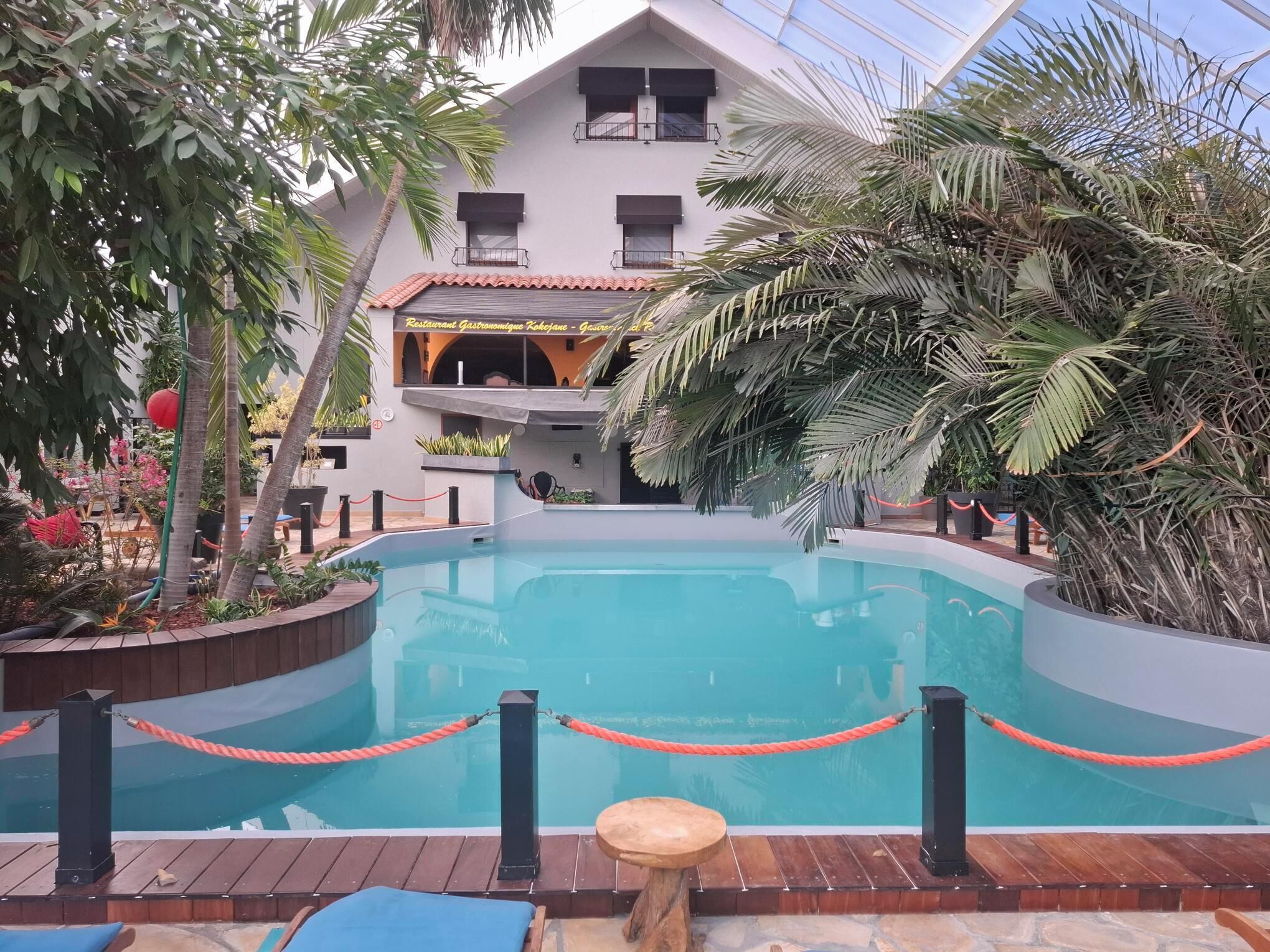 A pool area with a wooden deck, a red rope barrier, and a building with balconies in the background.