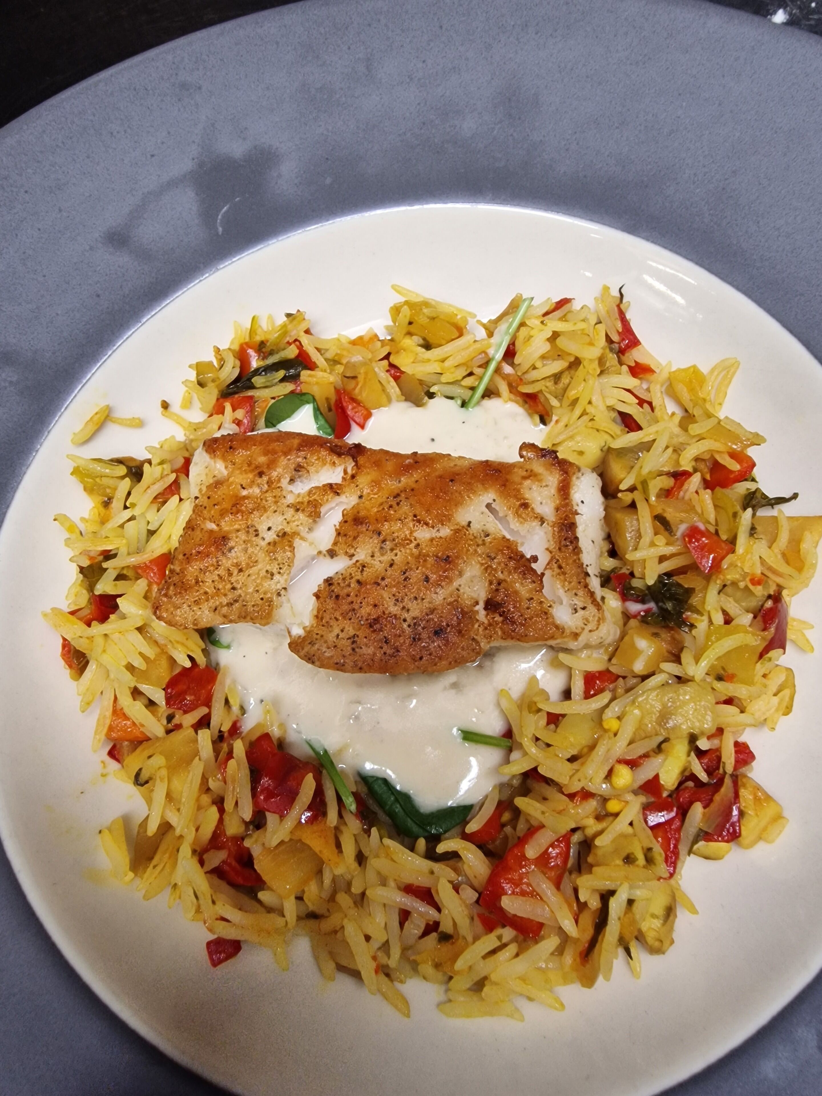 Un plato de comida con arroz, verduras y un trozo de pescado.