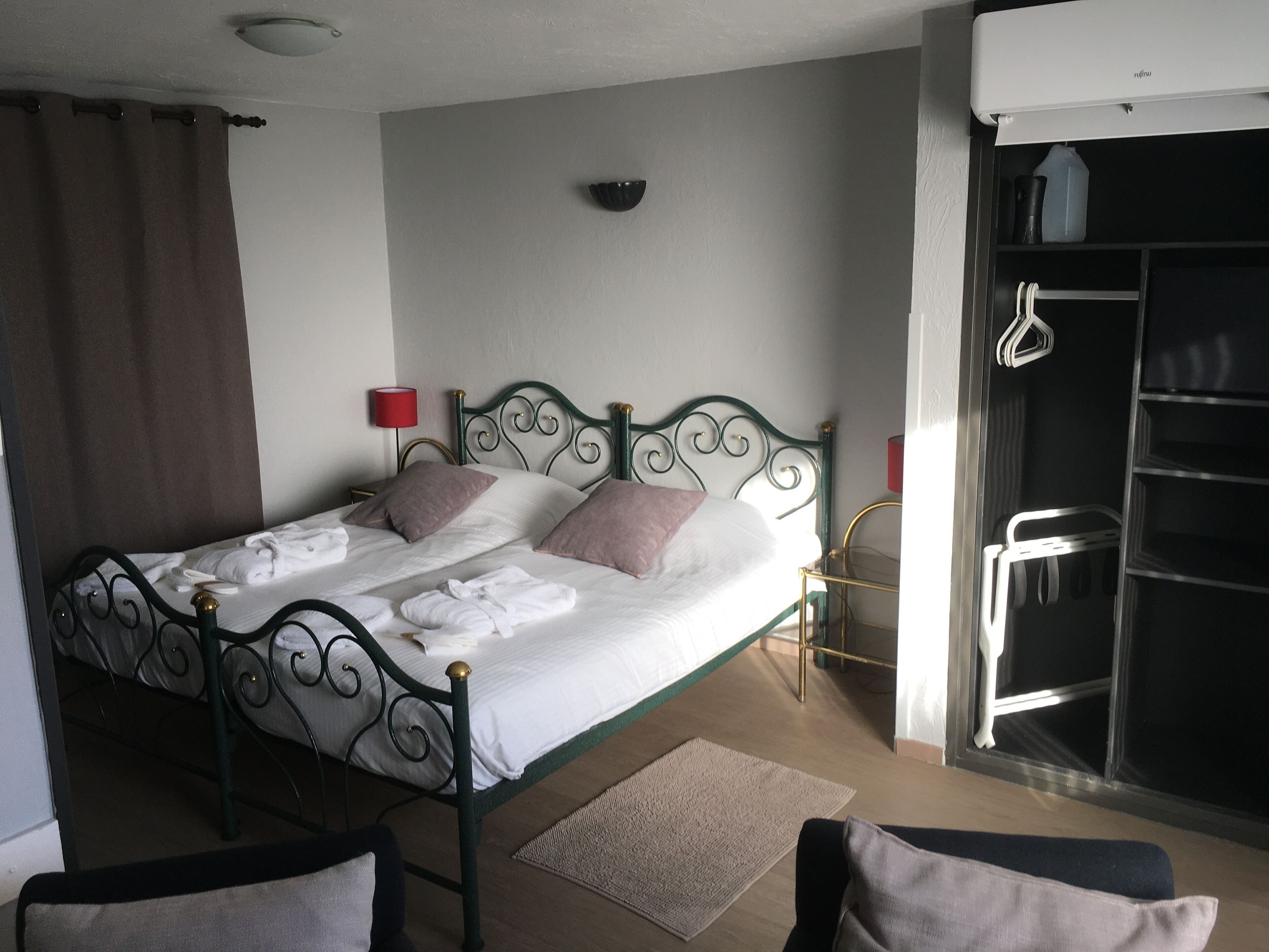 A neatly made bed with pillows, a bedside table with a lamp, a wardrobe, and a chair in a hotel room.
