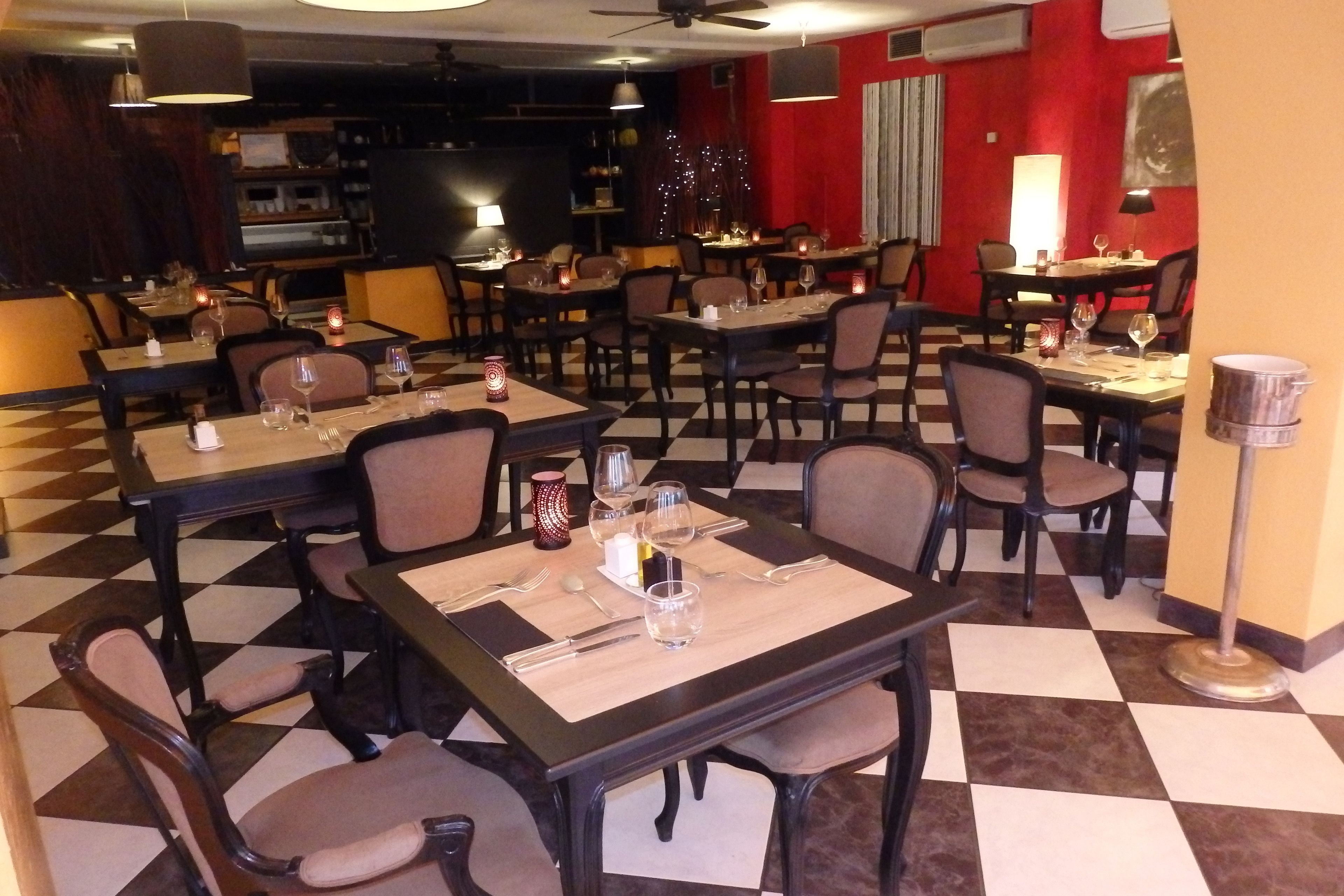 Een restaurant met geruit vloerkleed, meerdere tafels en stoelen, en een rode accentmuur.