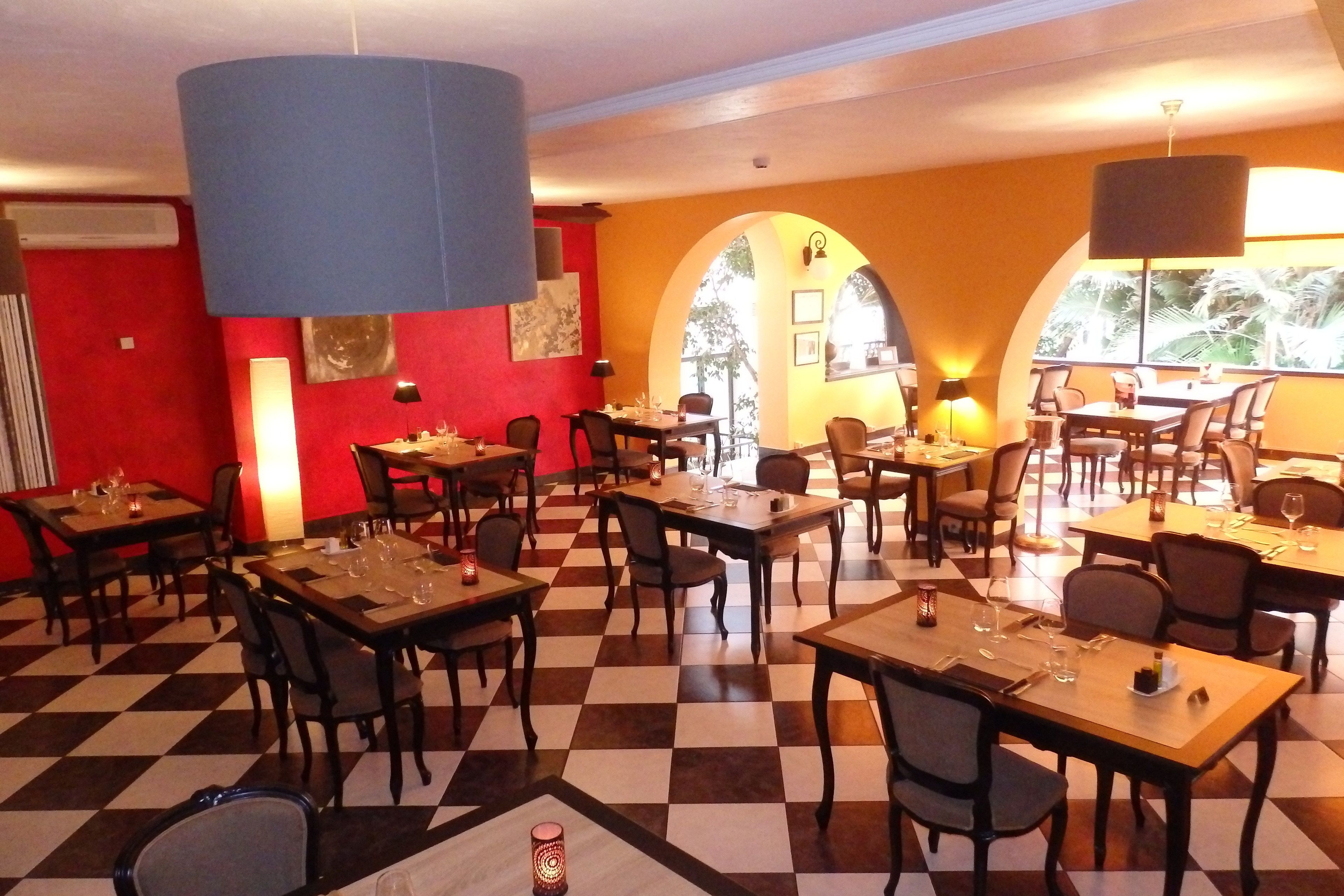 Een restaurant met schakerend vloerkleed, meerdere tafels en stoelen, en grote ramen met natuurlijk licht.