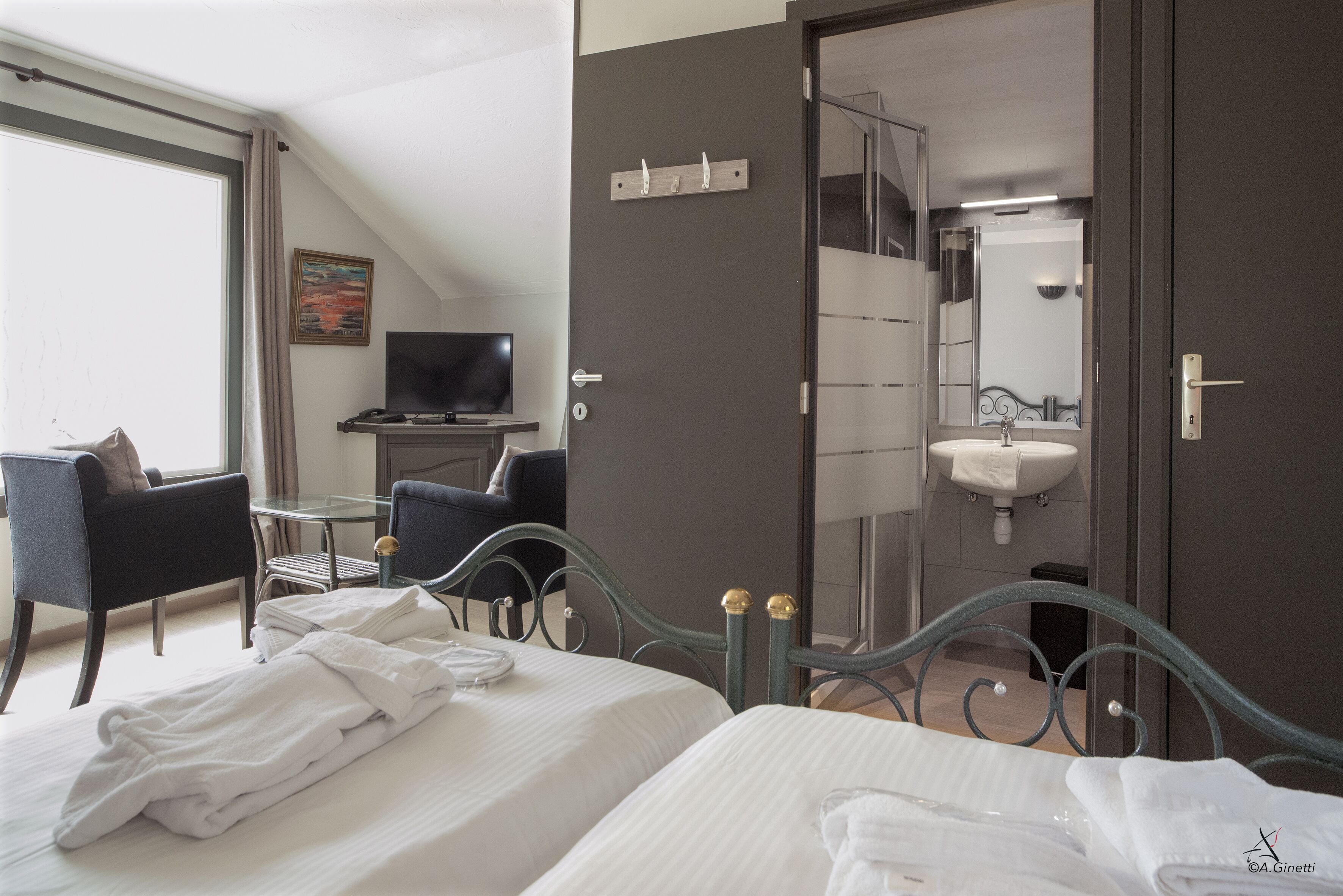 Hotelkamer met twee bedden, een bureau met stoel, een televisie en een badkamer met wastafel en spiegel.
