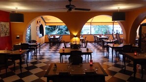 Un restaurante con suelo de tablones, mesas dispuestas para comer y ventanas arqueadas que dejan entrar luz natural.