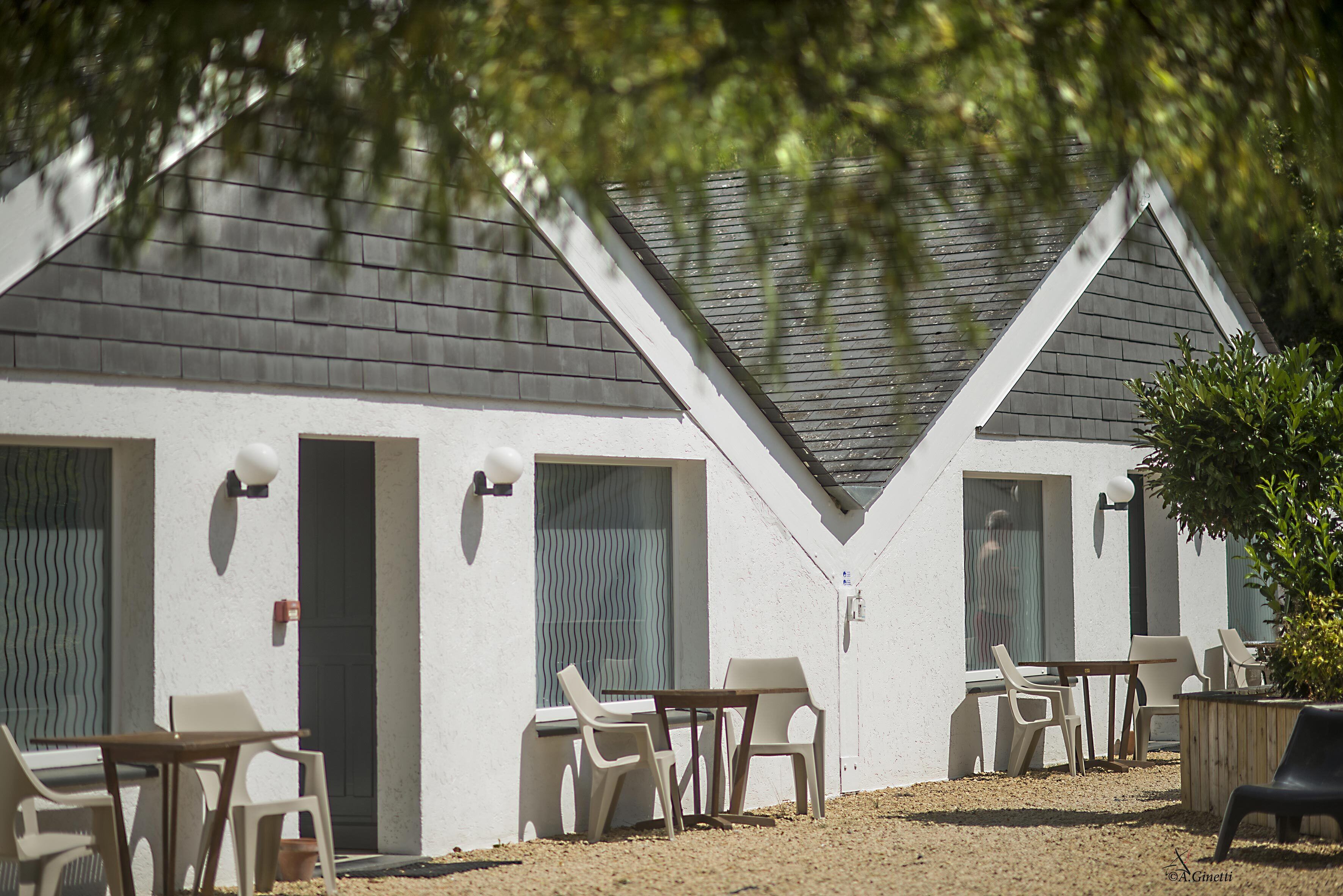 Un bâtiment à l’extérieur blanc et au toit foncé, doté de deux ensembles de mobilier d’extérieur comprenant des chaises et des tables en plastique blanc.