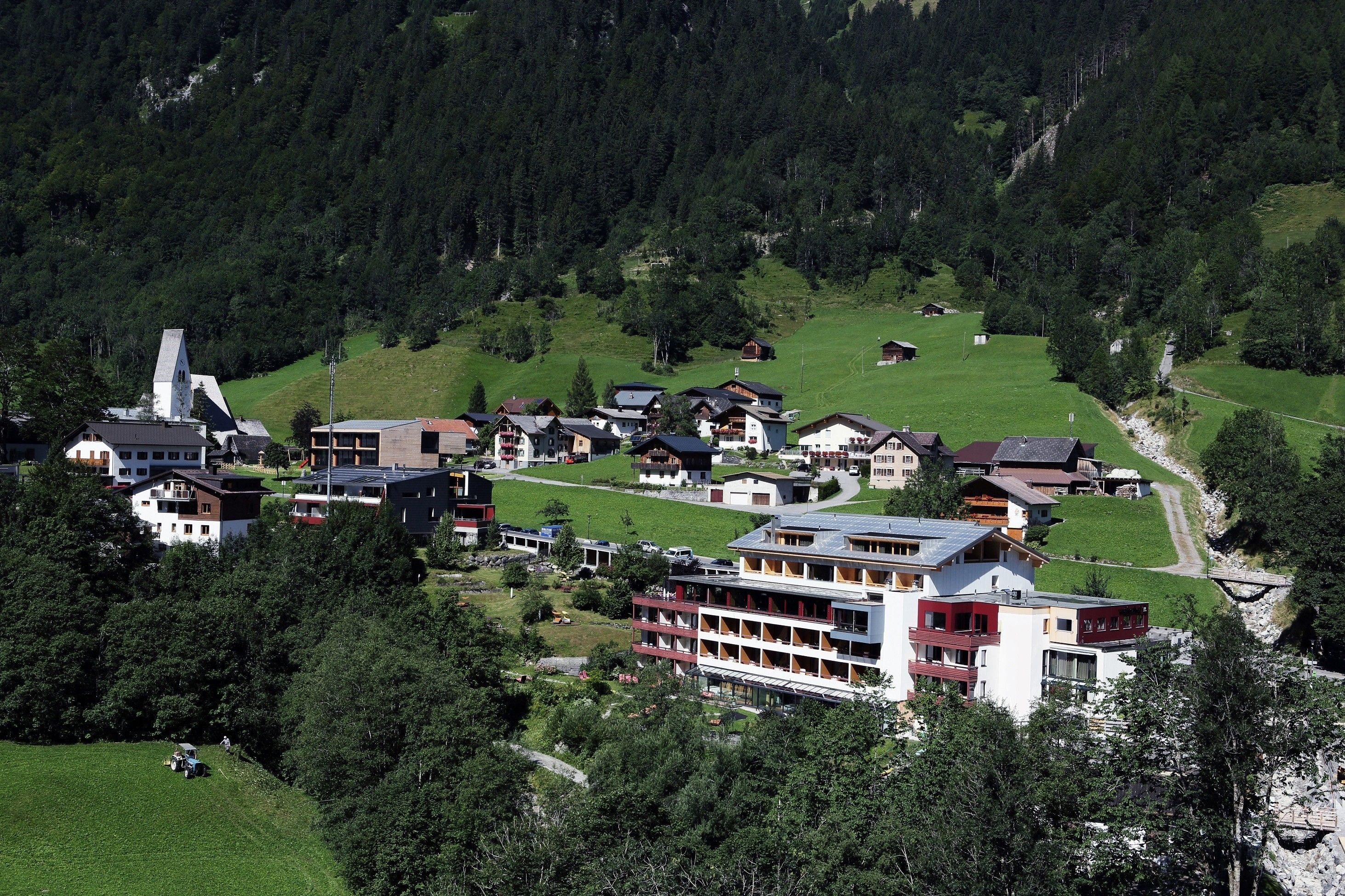 Un pueblo montañoso con una mezcla de construcciones tradicionales y modernas, incluyendo un hotel destacado con varios pisos y balcones.
