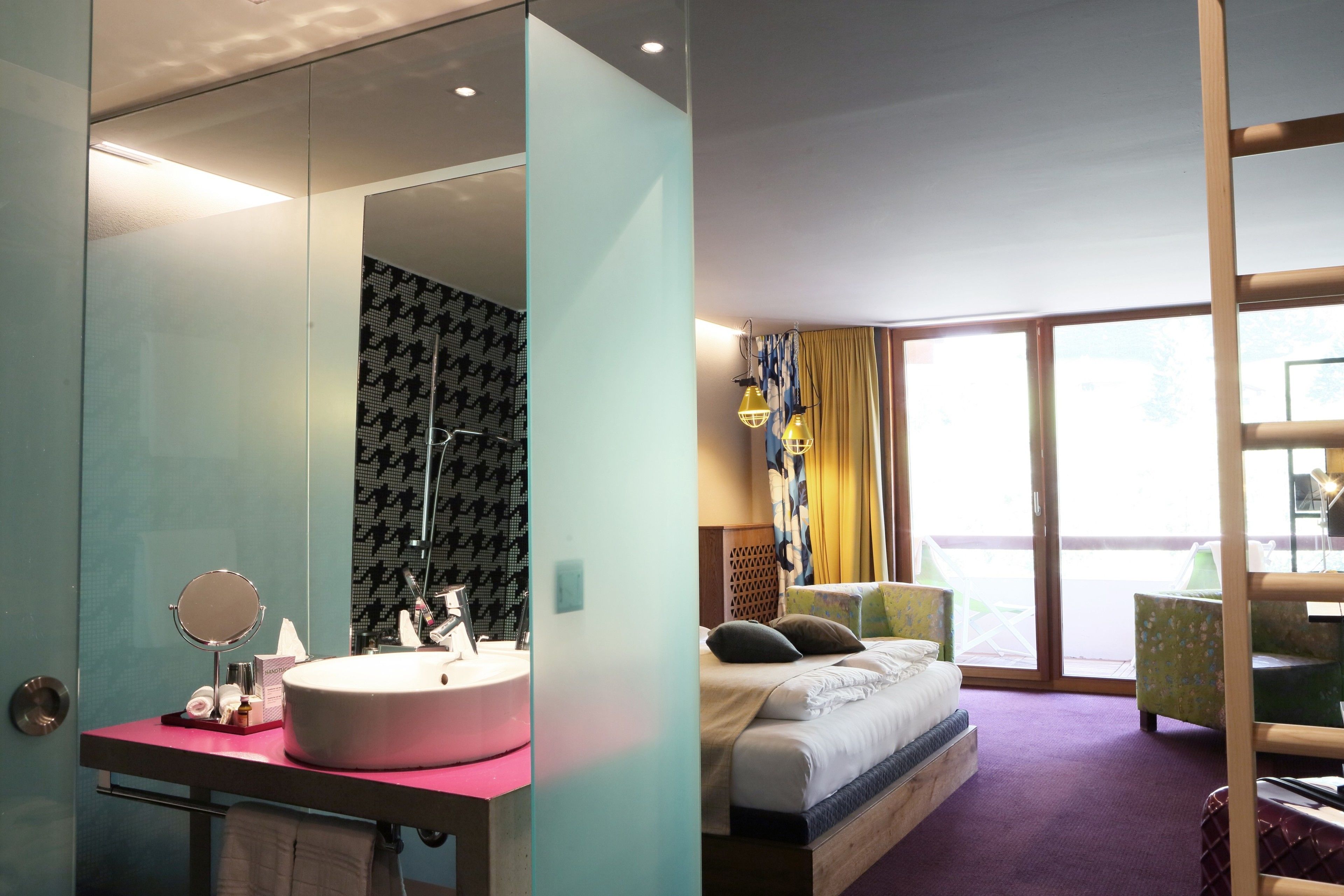 A hotel room with a large mirror, a round sink, a bed with pillows, and a view through a large window.