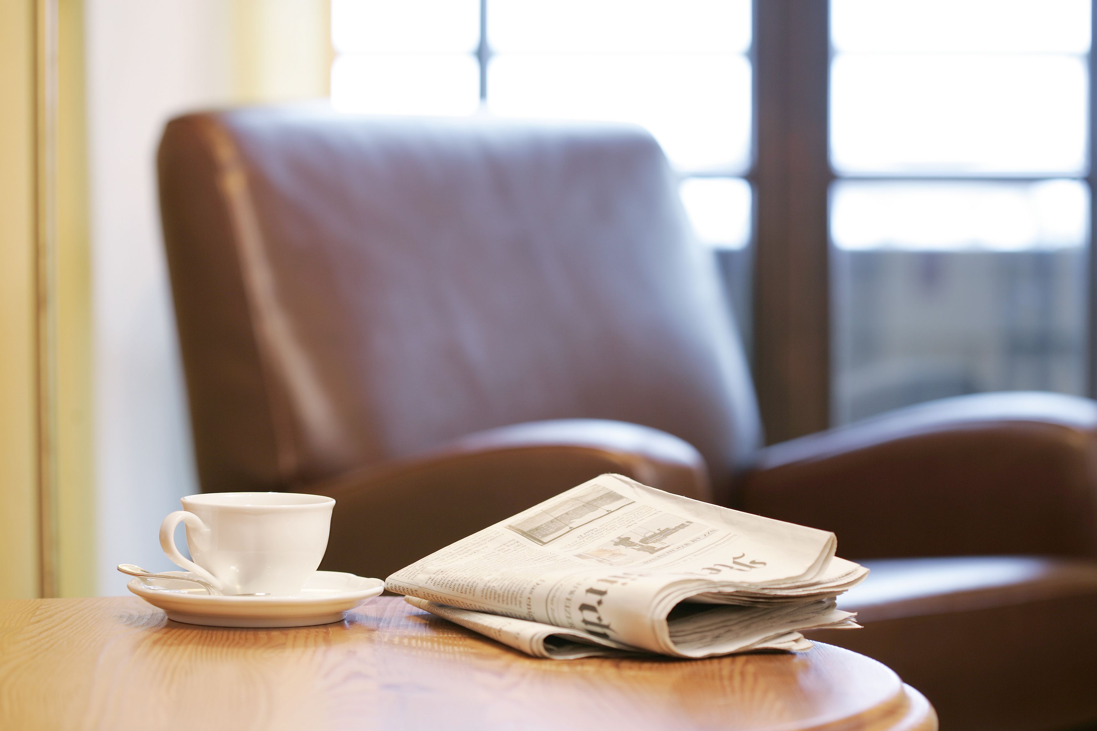 A cup and saucer on a wooden table with a newspaper beside it.