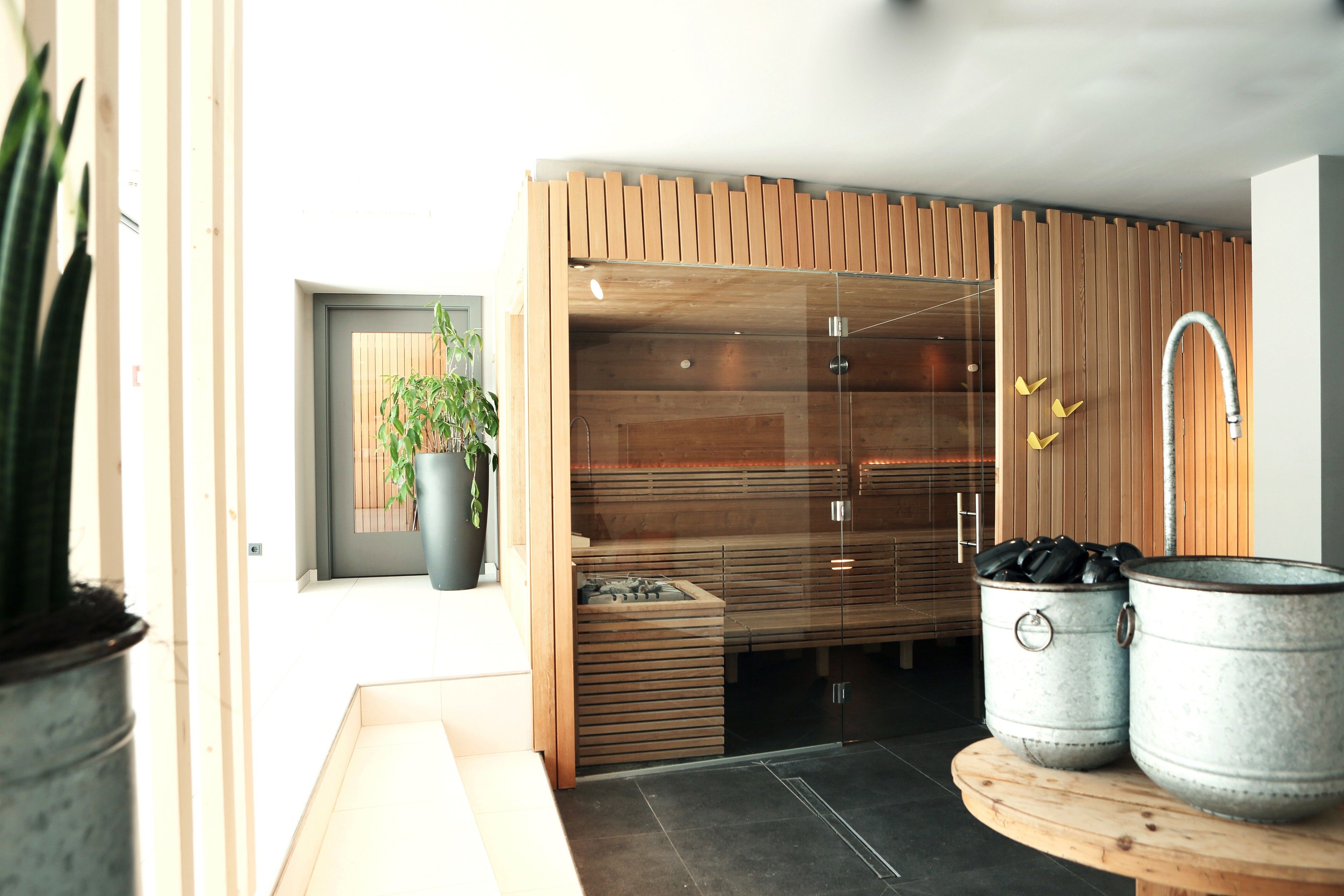 Un baño moderno con pared de paneles de madera, cabina de ducha de vidrio y dos cubos de metal sobre una mesa de madera.