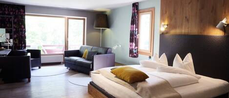 A modern hotel room with a large bed, a sofa, a desk, and a view of the outdoors.