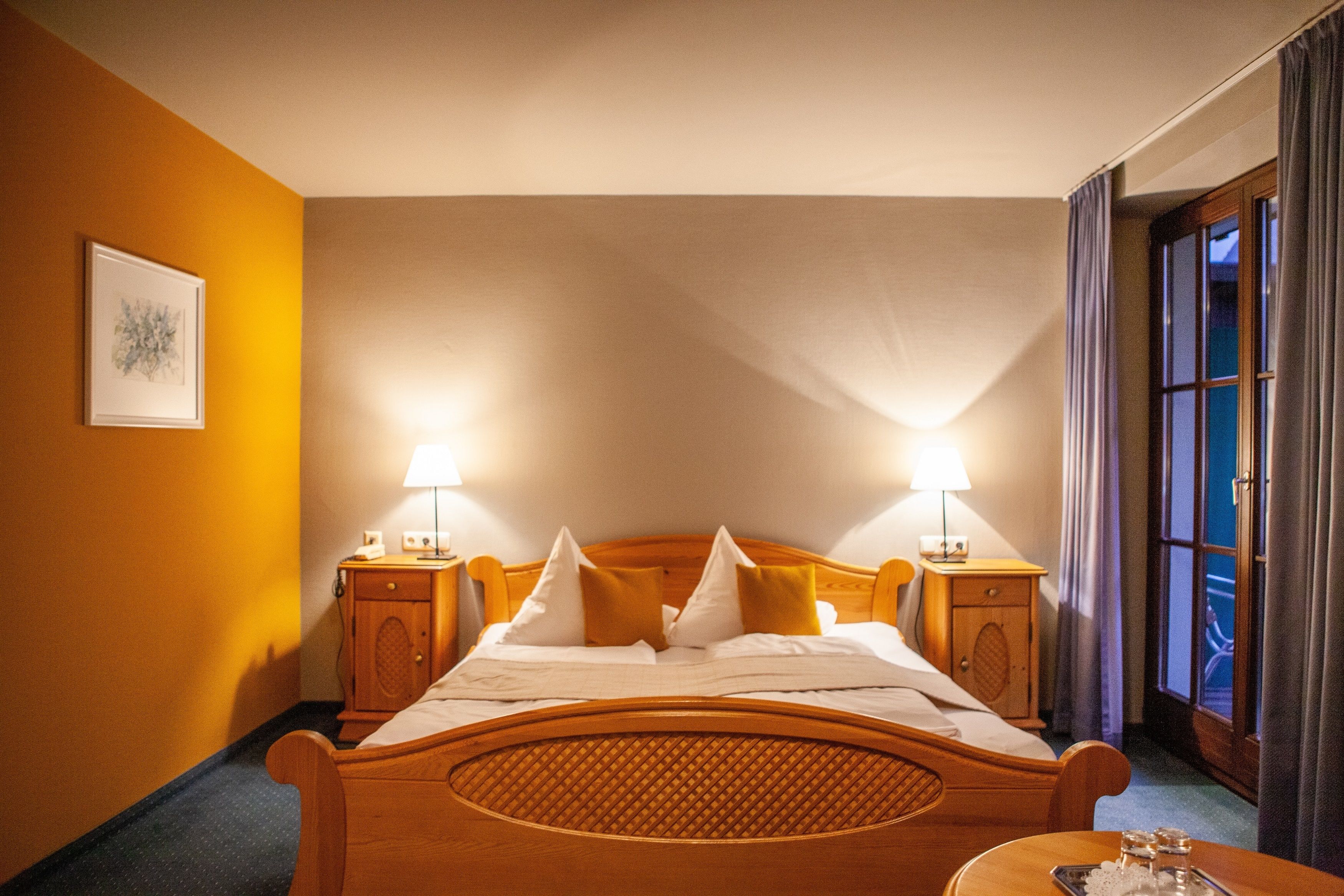 Ein Hotelzimmer mit einem Holzbett, zwei Nachttischen mit Lampen, einem Fenster mit Vorhängen und einem gerahmten Bild an der Wand.