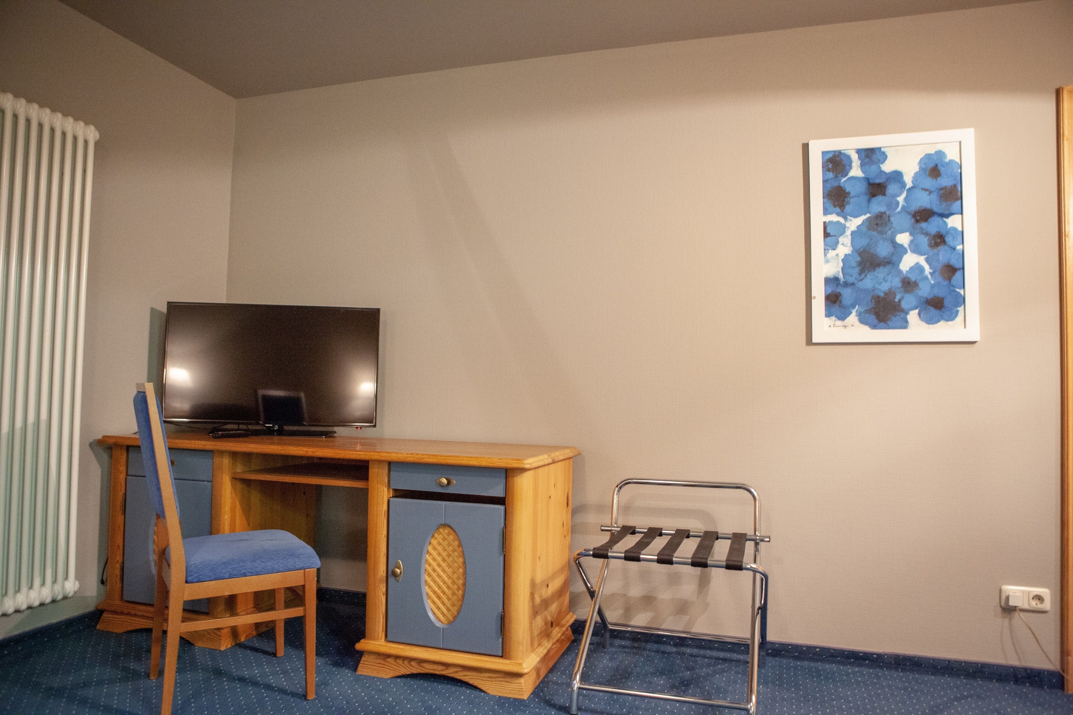 Una habitación con un escritorio de madera, una silla, un televisor, un radiador y un cuadro en la pared.