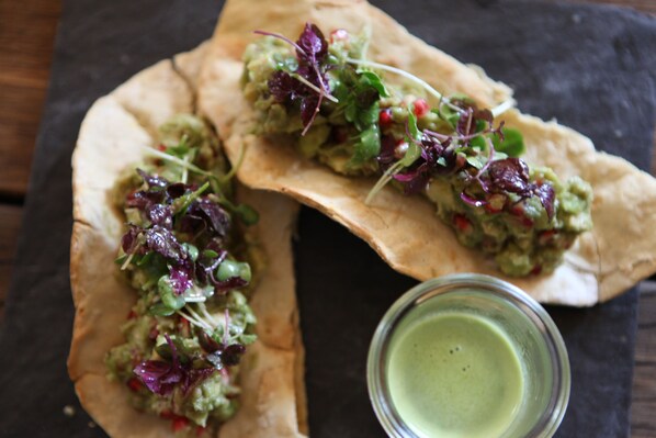 Two open-faced sandwiches with greens and a small bowl of green sauce.