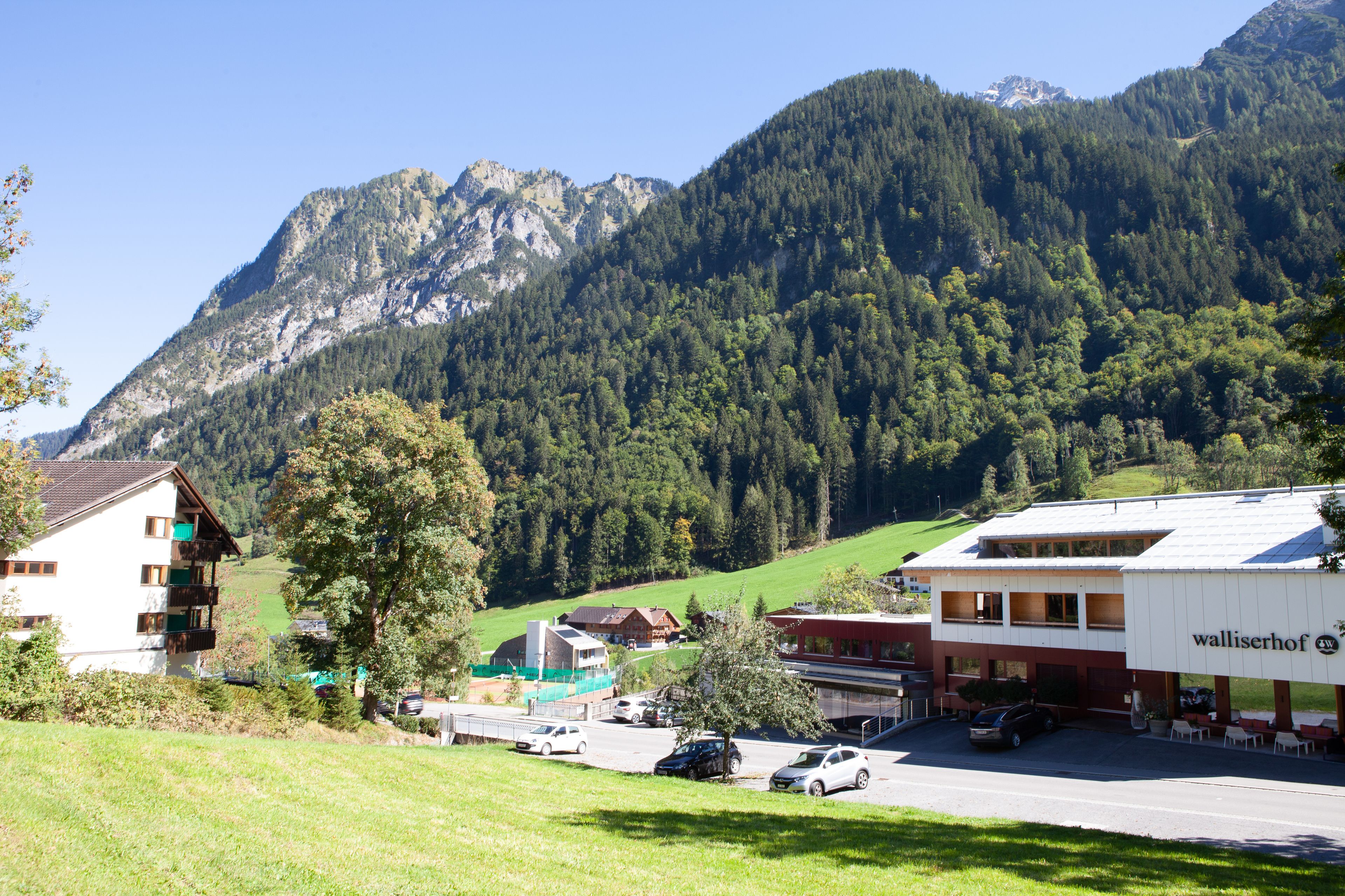 A hotel with a mountain backdrop, a parking area, and a building with a sign "walliserrhof".