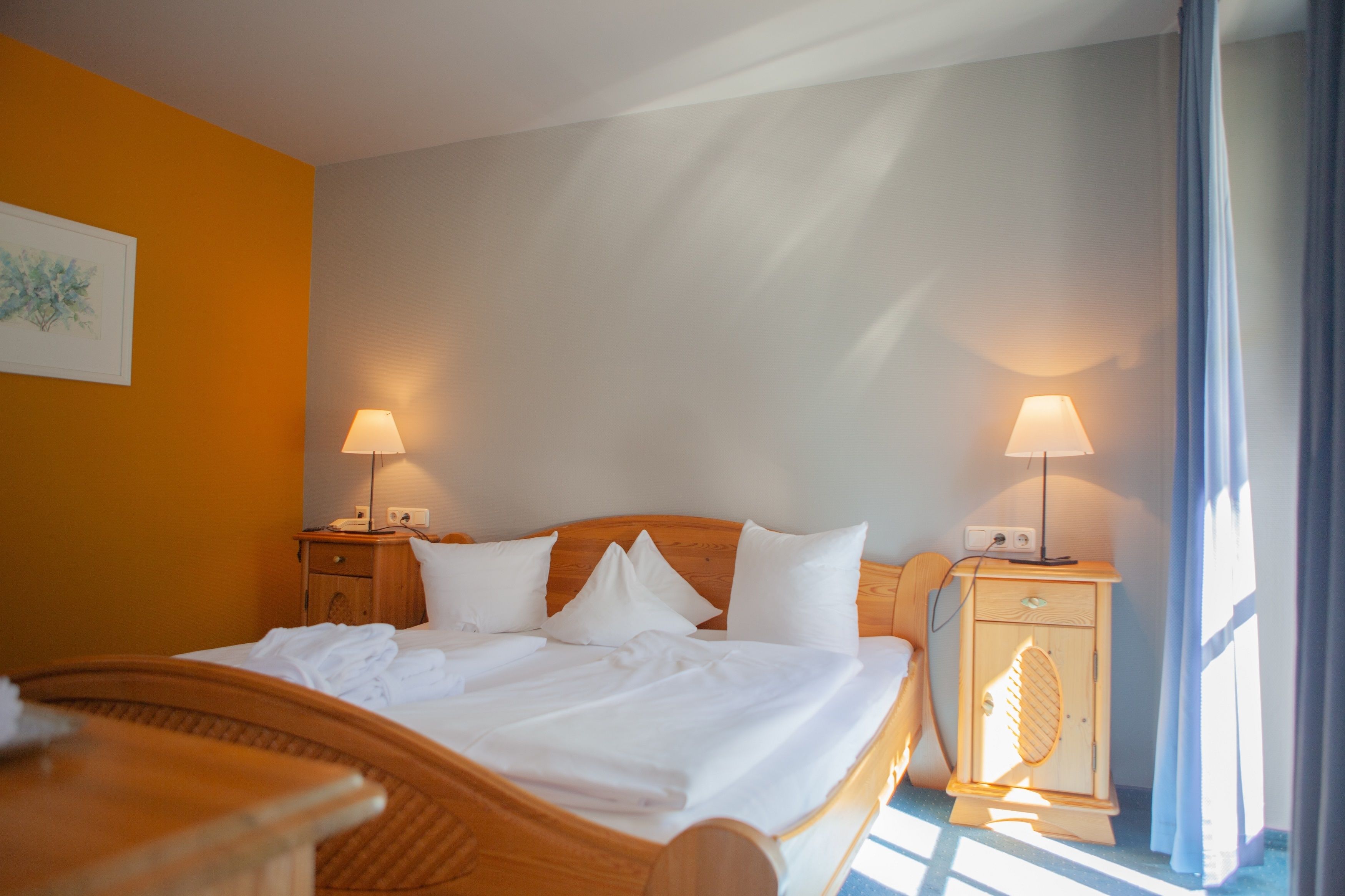 A hotel room with a bed, two bedside lamps, a nightstand, and a wall-mounted lamp.