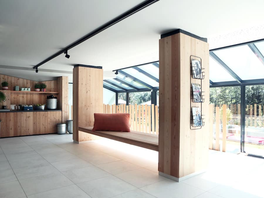 A modern interior with a wooden bench, skylights, and a kitchen area with potted plants.