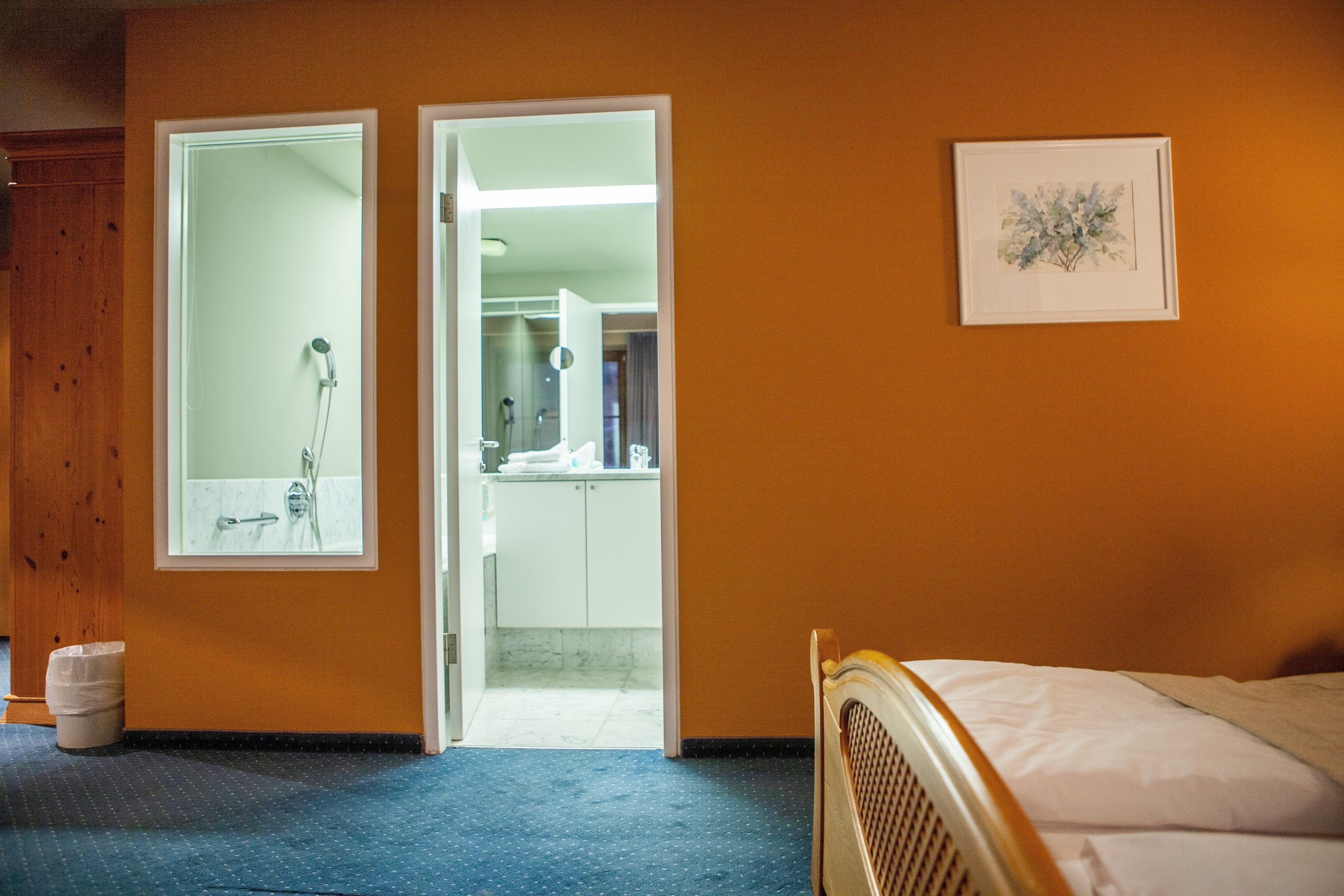 A hotel room with a bed, a bathroom with a shower, a sink, and a framed picture on the wall.