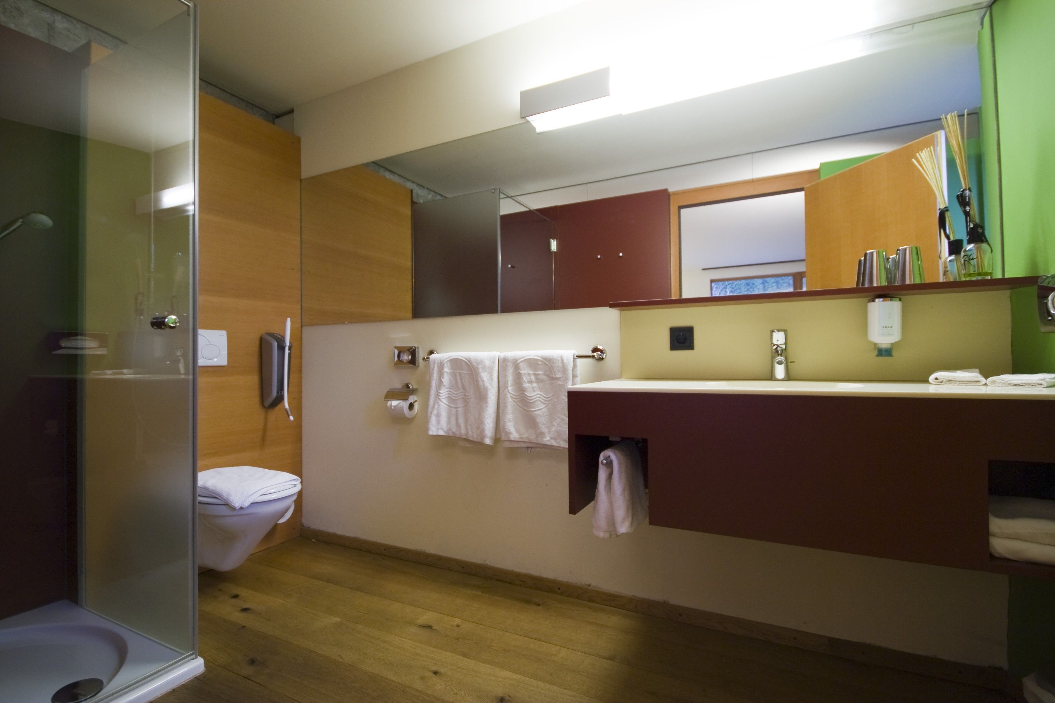 Ein Badezimmer mit Glasdusche, Toilette, Waschbecken inklusive Spiegel und einem Handtuchhalter.