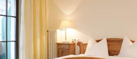 A hotel room with a wooden bed, a nightstand with a lamp, and a window with curtains.