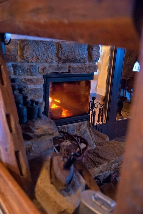 Una chimenea de piedra con fuego encendido, rodeada de leña y una rejilla metálica.