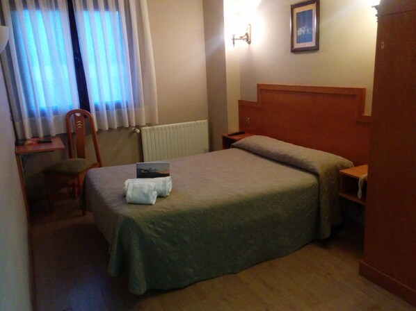 Una habitación de hotel con cama, una silla, un escritorio y un radiador.